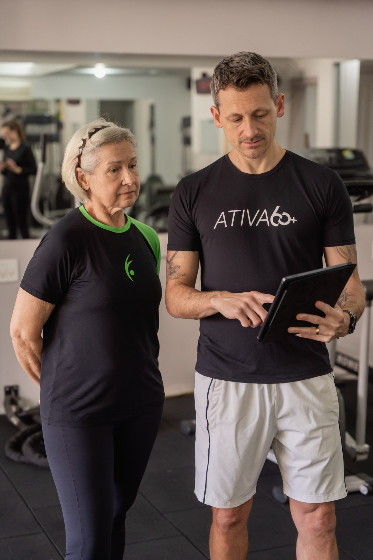 Personal trainer explicando o treino para aluna de 60+ usando um tablet